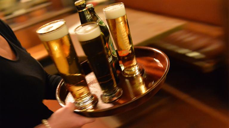 Eine Bedienung trägt in einem Lokal ein Tablett mit Bier.