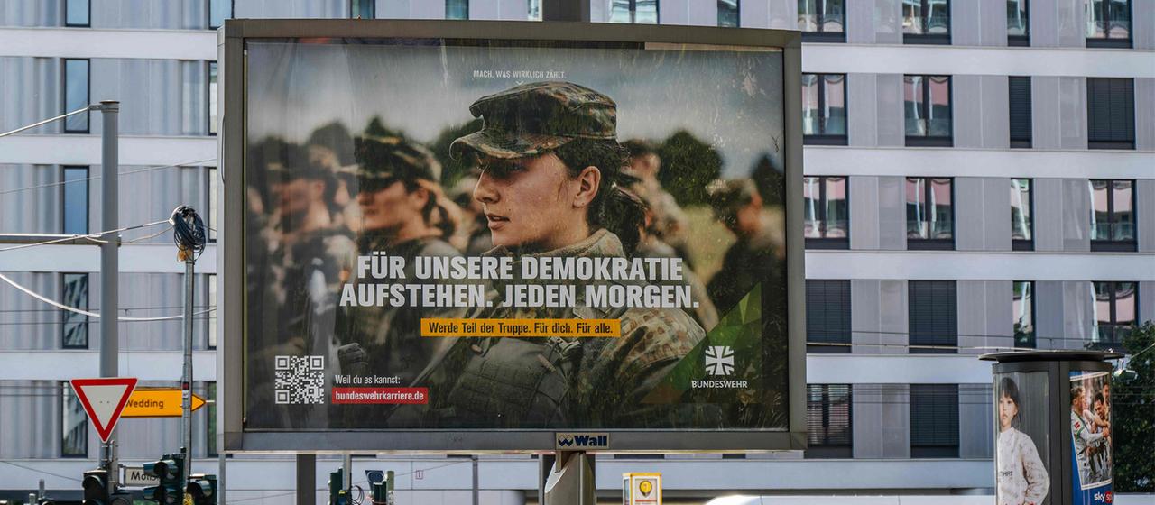 Ein Plakat mit einer Bundeswehrsoldatin und der Aufschrift "Für unsere Demokratie aufstehen. Jeden Morgen." hängt in Berlin. | AFP Ein Plakat mit einer Bundeswehrsoldatin und der Aufschrift "Für unsere Demokratie aufstehen. Jeden Morgen." hängt in Berlin.