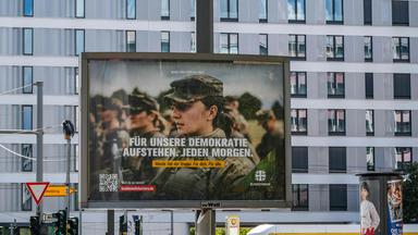 Ein Plakat mit einer Bundeswehrsoldatin und der Aufschrift "Für unsere Demokratie aufstehen. Jeden Morgen." hängt in Berlin.