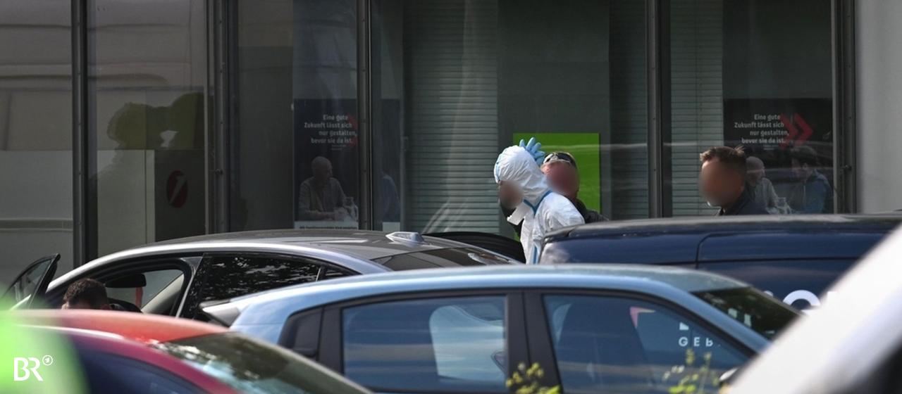 Eine Person in einem speziellen, weißen Anzug wird bei einem Polizeieinsatz an einer Bank weggeführt.