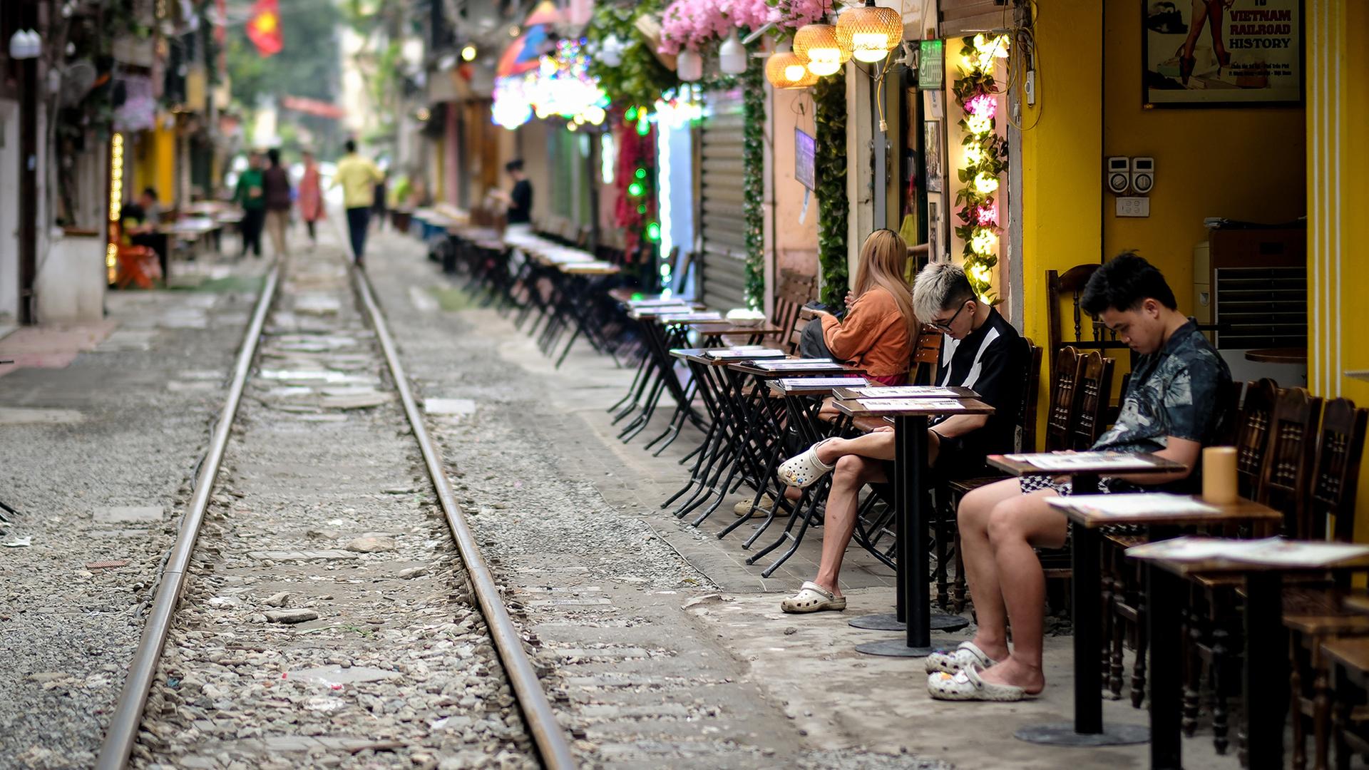 Menschen sitzen in einem CafÃ© in Hanoi, das direkt an Bahngleisen liegt. | EPA