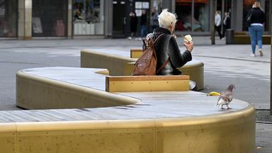 Eine Frau und eine Taube auf einer goldglänzenden Bank in der Fussgängerzone von Elberfeld.