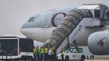 Menschen besteigen ein Flugzeug der Qatar Airways, vor dem Beamte der Bundespolizei stehen