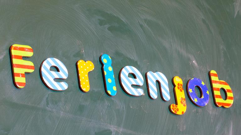 An einer Schultafel steht in bunten Buchstaben das Wort "Ferienjob".