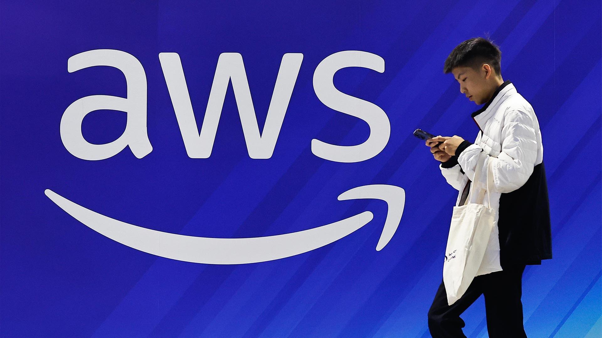 Ein Mann geht an einer Wand mit dem Logo von Amazon Web Services (AWS) vorbei. | picture alliance / Anadolu