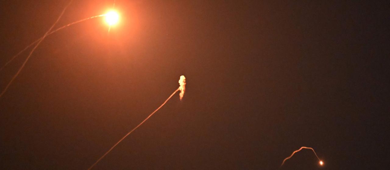 Am Nachthimmel sind Leuchtspuren und Explosionen von Raketen zu sehen.