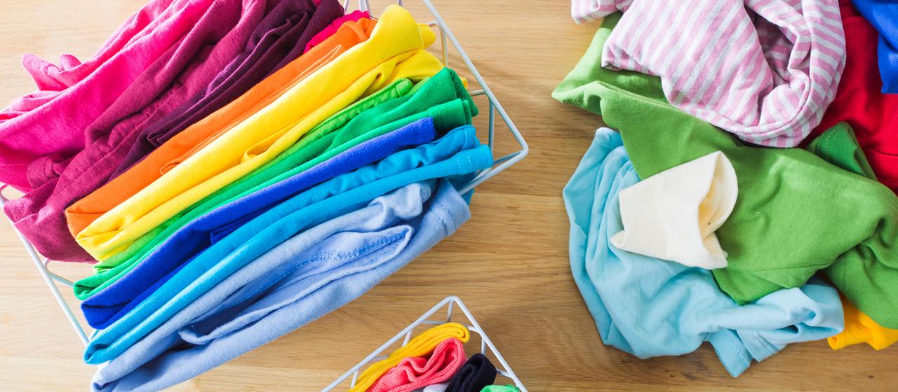 Bunte Kleidung liegt ordentlich in Boxen und auf dem Boden.