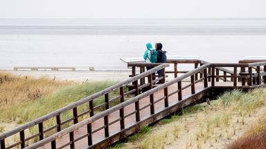 Zwei Frauen stehen bei regnerischem Wetter auf einer Aussichtsplattform am Strand und schauen auf die Nordsee.