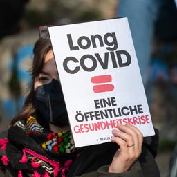 Eine Frau hält ein Plakat mit der Aufschrift "Long Covid = eine öffentliche Gesundheitskrise"