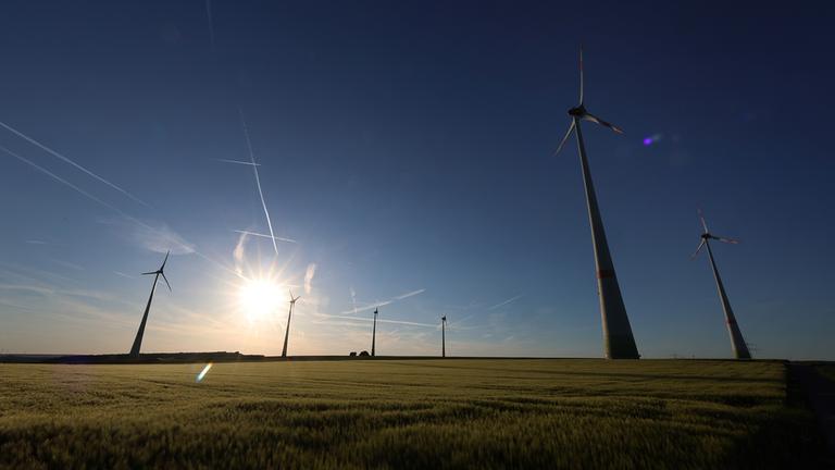Windräder stehen in der Abendsonne hinter einem Getreidefeld in Sommerhausen (Bayern).