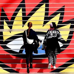 Zwei junge Frauen laufen eine Treppe hinauf, auf der das Logo der Leipziger Buchmesse zu sehen ist.