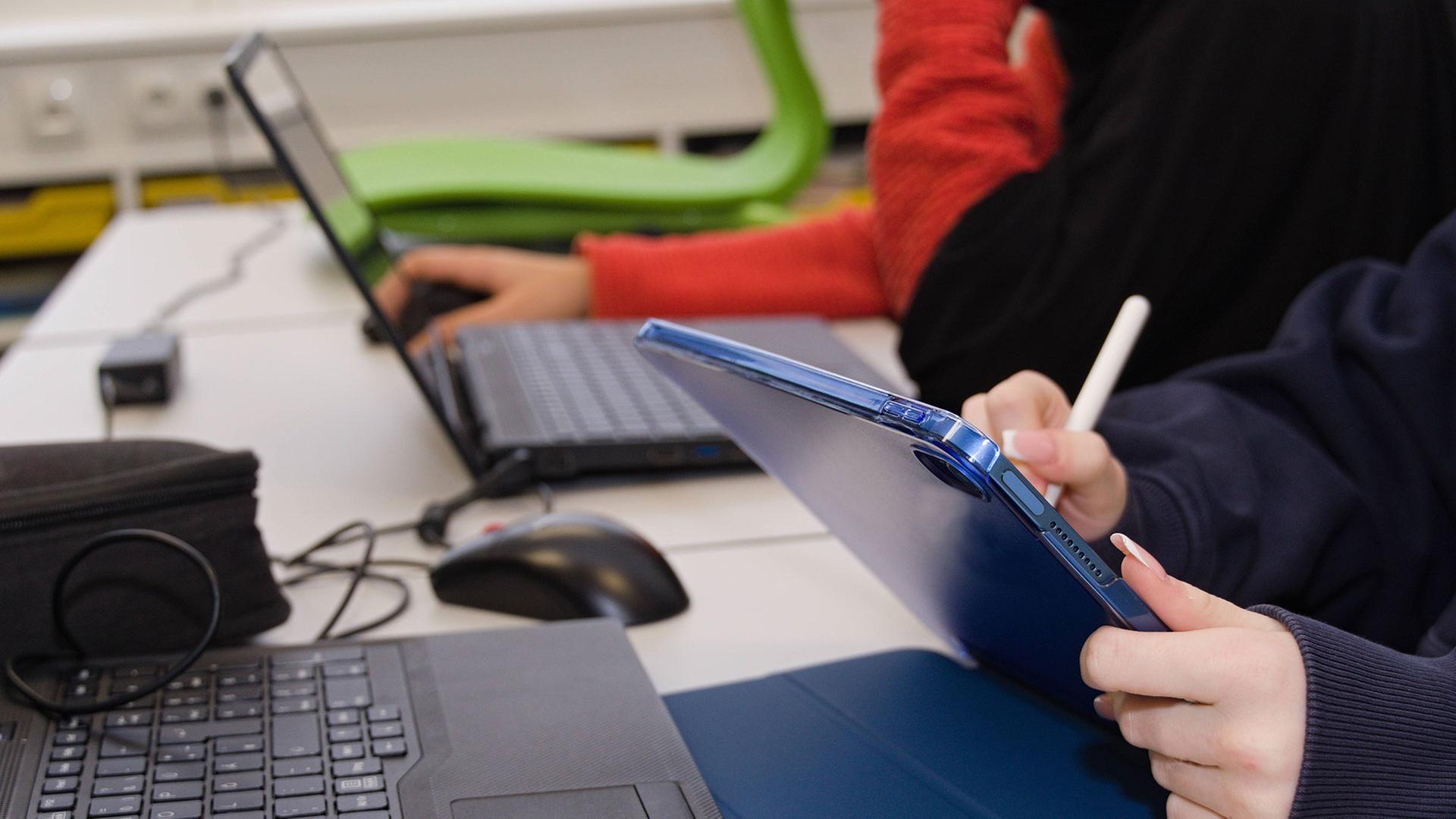 Schüler schreiben auf einem Tablet und arbeiten an einem Laptop. | IMAGO / CHROMORANGE