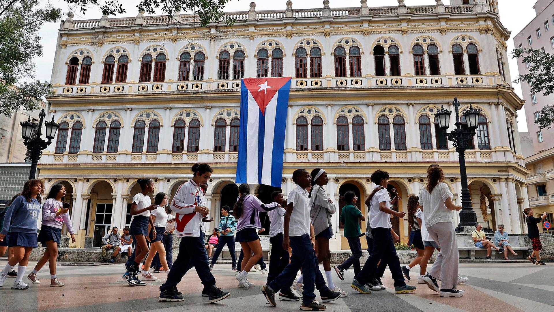 Menschen gehen in Havanna an einem Gebäude mit der kubanischen Flagge vorbei. | EPA