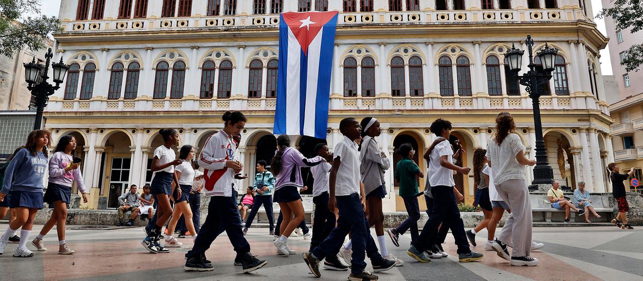 Menschen gehen in Havanna an einem Gebäude mit der kubanischen Flagge vorbei.