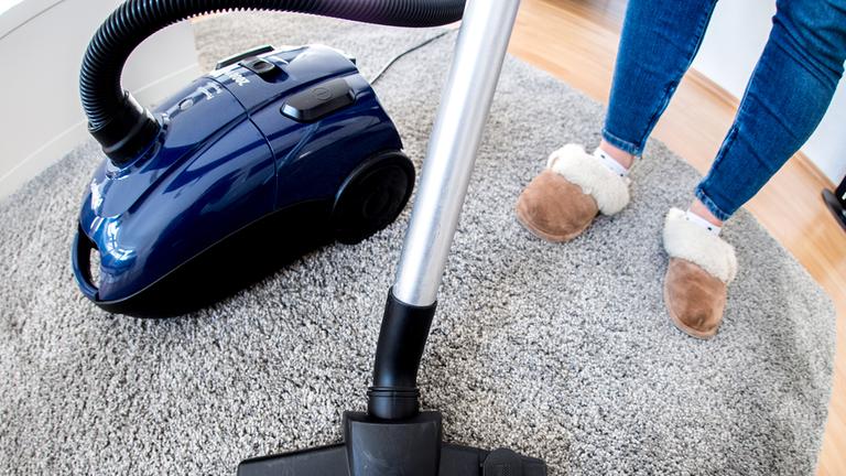 Eine Frau saugt in einer Wohnung einen Teppich mit einem Staubsauger.