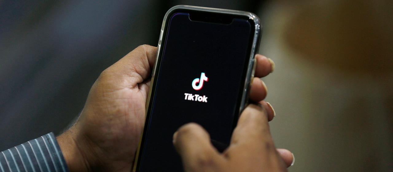 Ein Mann hält ein Handy in seiner Hand. Auf dem Bildschirm ist die App Tiktok zu sehen.