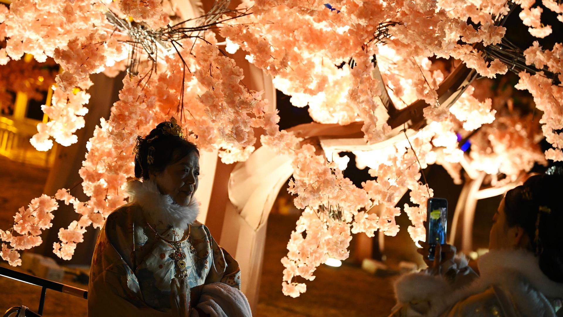 Eine Frau steht unter einem beleuchteten Baum. | Johannes Neudecker/dpa