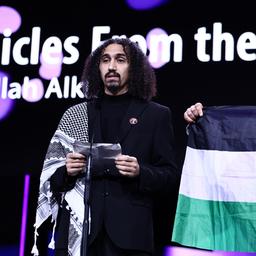 Abdallah Alkhatib (l), Regisseur vom Film "Chronicles from the Siege" spricht bei der Übergabe des GWFF Preis Bestes Spielfilmdebüt während der Preisverleihung bei der Abschlussgala im Berlinale Palast auf der Bühne. Neben ihm wird die palästinensische Fahne hochgehalten. (Quelle: dpa/Soeder)