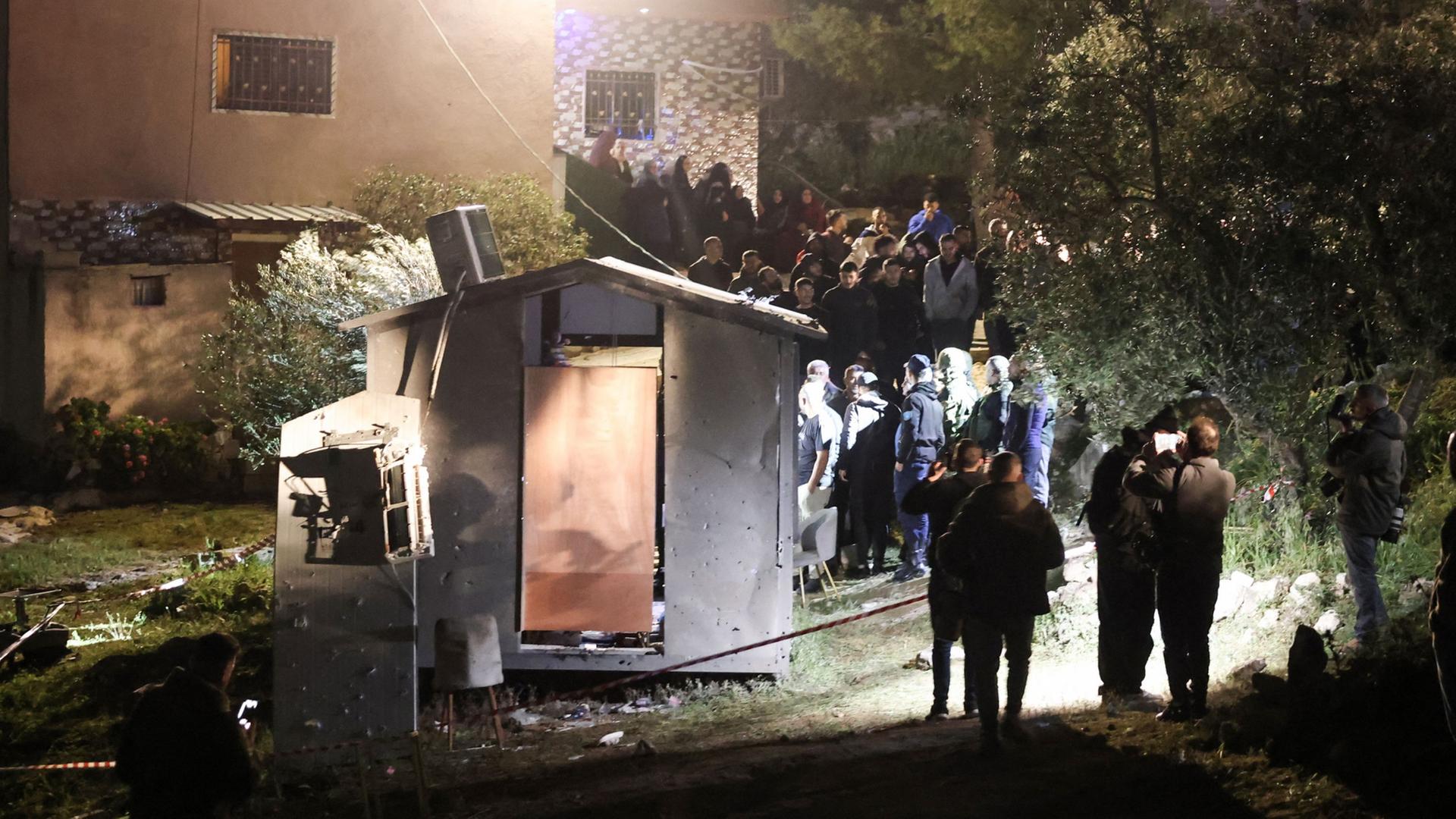 Menschen stehen nachts in Beit Awa im Westjordanland vor einem Haus, dass durch einen Angriff beschÃ¤digt wurde. | AFP