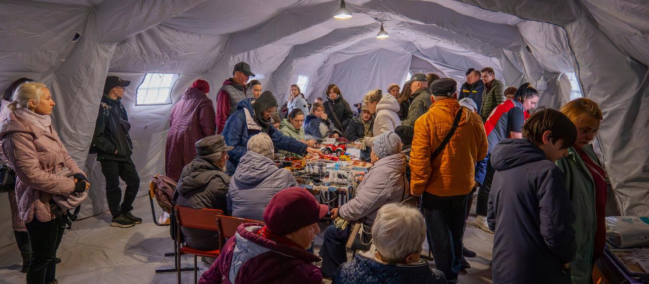 Menschen suchen nach einem russischen Angriff in der Region Tschernihiw Schutz in einem beheizten Zelt, das mit einem Notstromaggregat versorgt wird. | AP Menschen suchen nach einem russischen Angriff in der Region Tschernihiw Schutz in einem beheizten Zelt, das mit einem Notstromaggregat versorgt wird.