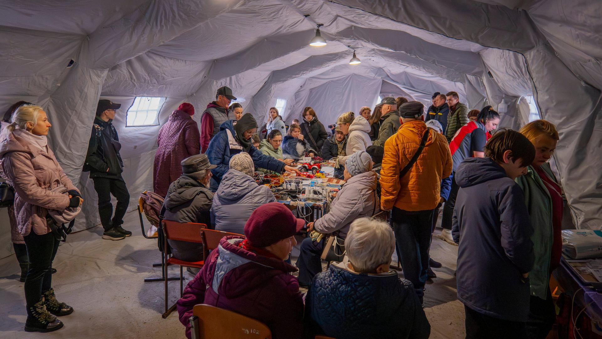 Menschen suchen nach einem russischen Angriff in der Region Tschernihiw Schutz in einem beheizten Zelt, das mit einem Notstromaggregat versorgt wird. | AP