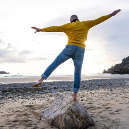 Ein Mann balanciert auf einem Bein auf einem Stein an einem Strand.
