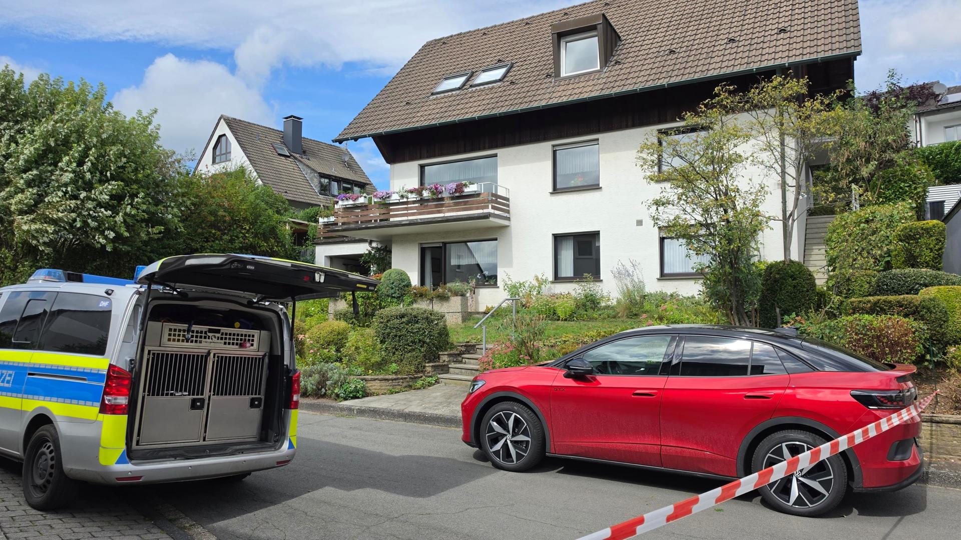 Ein Polizeiwagen und ein rotes Auto stehen hinter einer Polizeiabsperrung an einem Wohnhaus | WDR / Christof Voigt