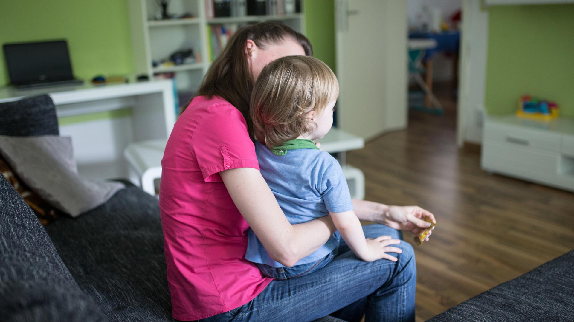 Eine Mutter sitzt mit ihrem Sohn auf dem Schoß auf einer Couch. | dpa