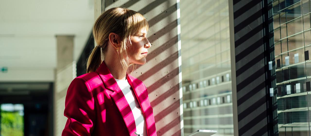Eine Frau mit Tablet-PC steht an einem Bürofenster.