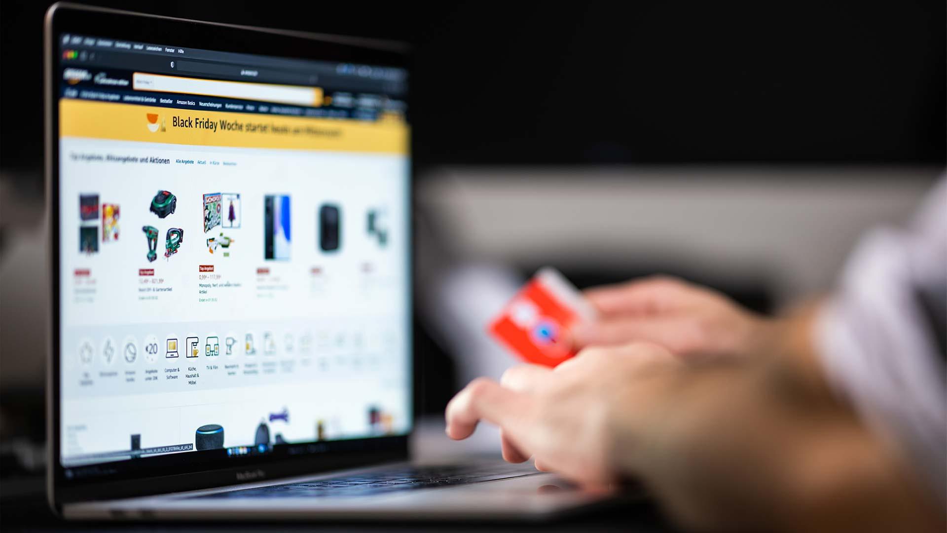 Eine Person, Bankkarte in der Hand, schaut am Laptop Black Friday Angebote an. | picture alliance/dpa