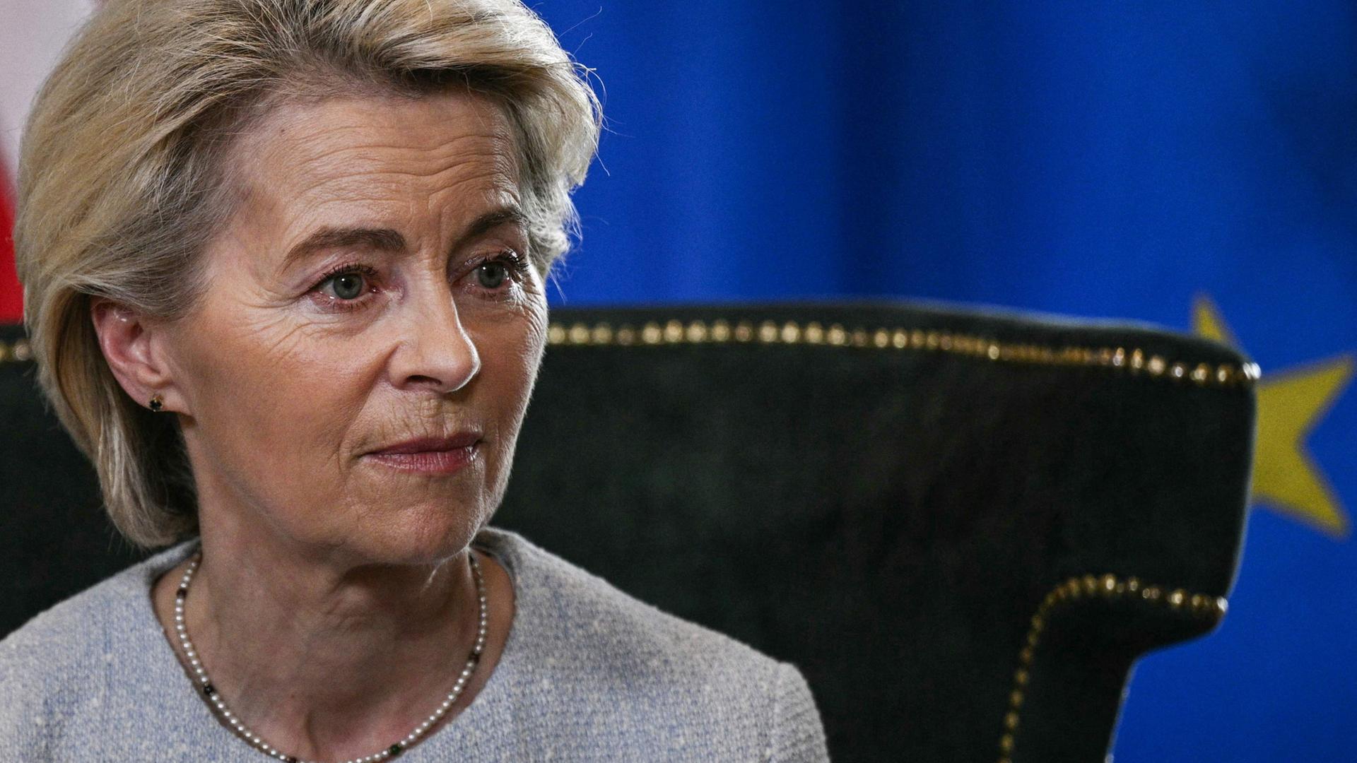 Ursula von der Leyen sitzt vor einer EU-Flagge. | AFP