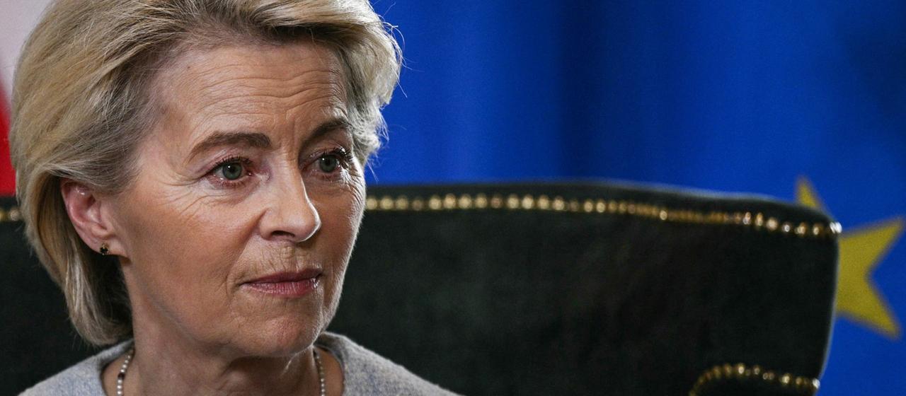 Ursula von der Leyen sitzt vor einer EU-Flagge.