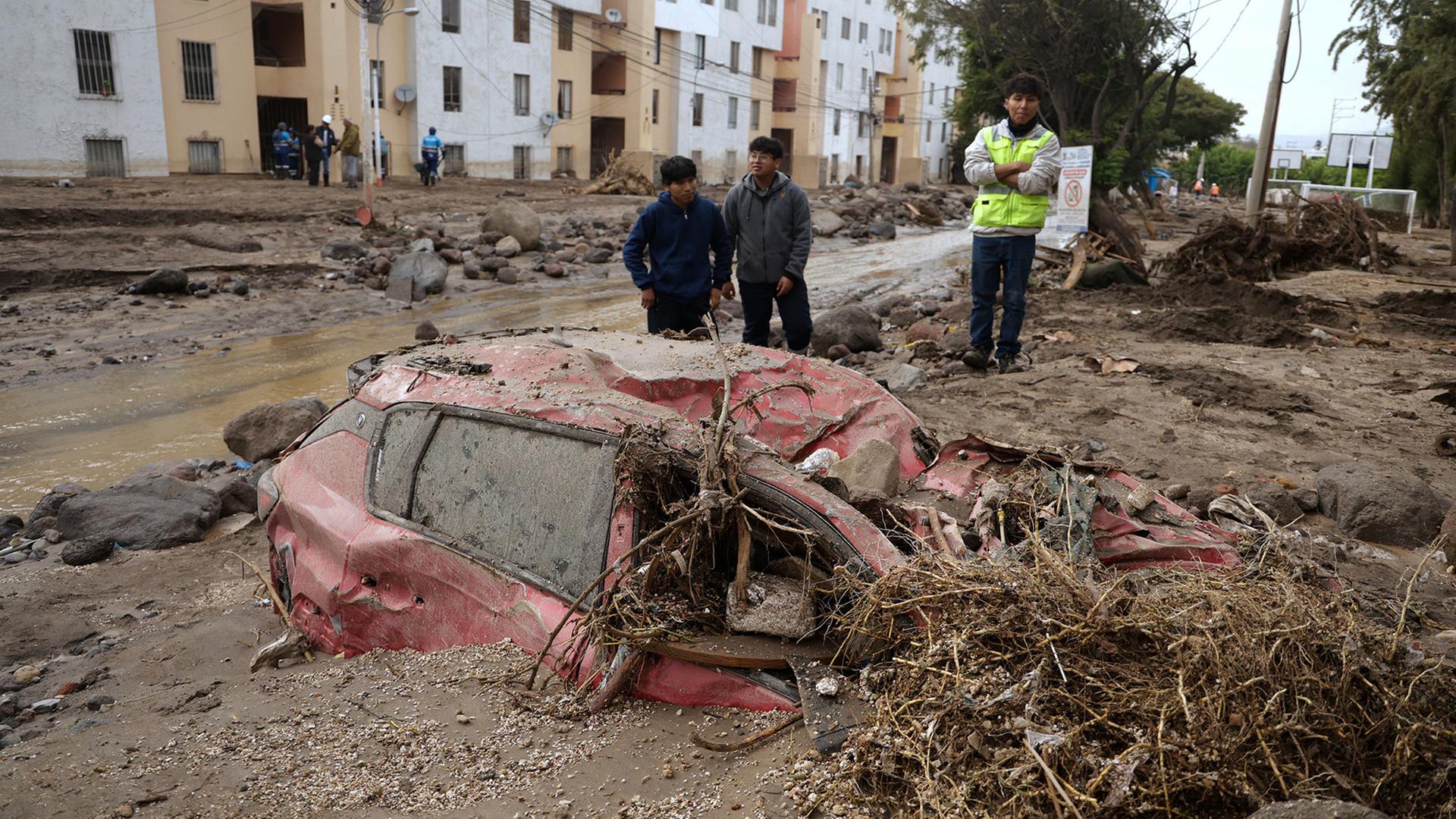 Menschen inspizieren nach Überschwemmungen die Straße, die durch starke Regenfälle zerstört wurde. | Jose Sotomayor/AP/dpa