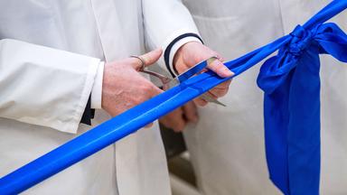 Ein blaues Band wird anlässlich einer Eröffnung mit einer Schere durchschnitten.