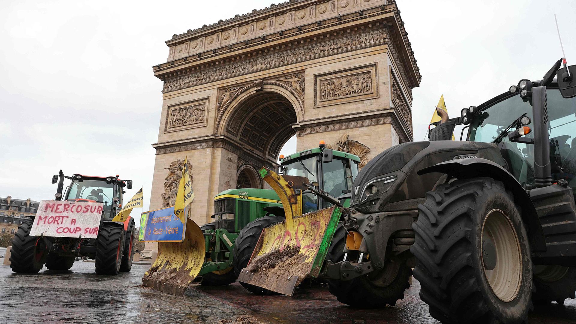 Traktoren mit Bannern auf den Schaufeln stehen vor dem Triumphbogen in Paris. | AFP