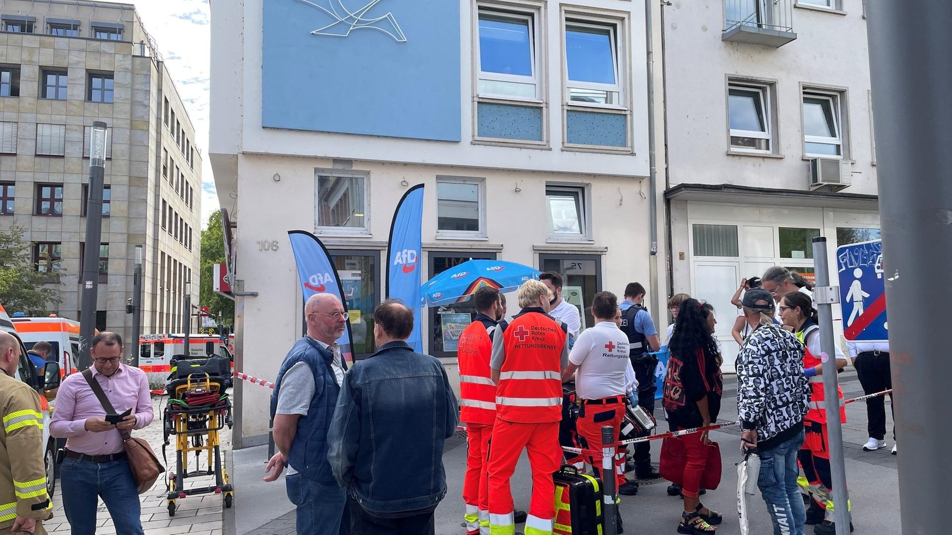 Mehrere Rettungskräfte und Polizisten stehen um einen Stand der AfD herum. Auf den Stand wurde eine Flüssigkeit geschüttet. | SWR, S. Jakobi