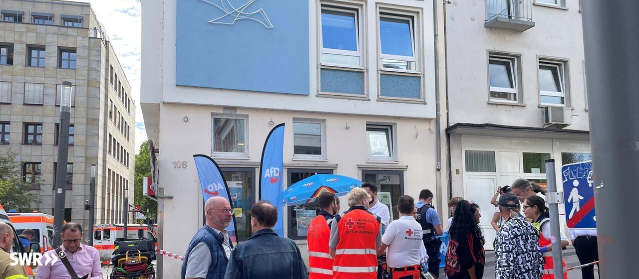 Mehrere Rettungskräfte und Polizisten stehen um einen Stand der AfD herum. Auf den Stand wurde eine Flüssigkeit geschüttet.
