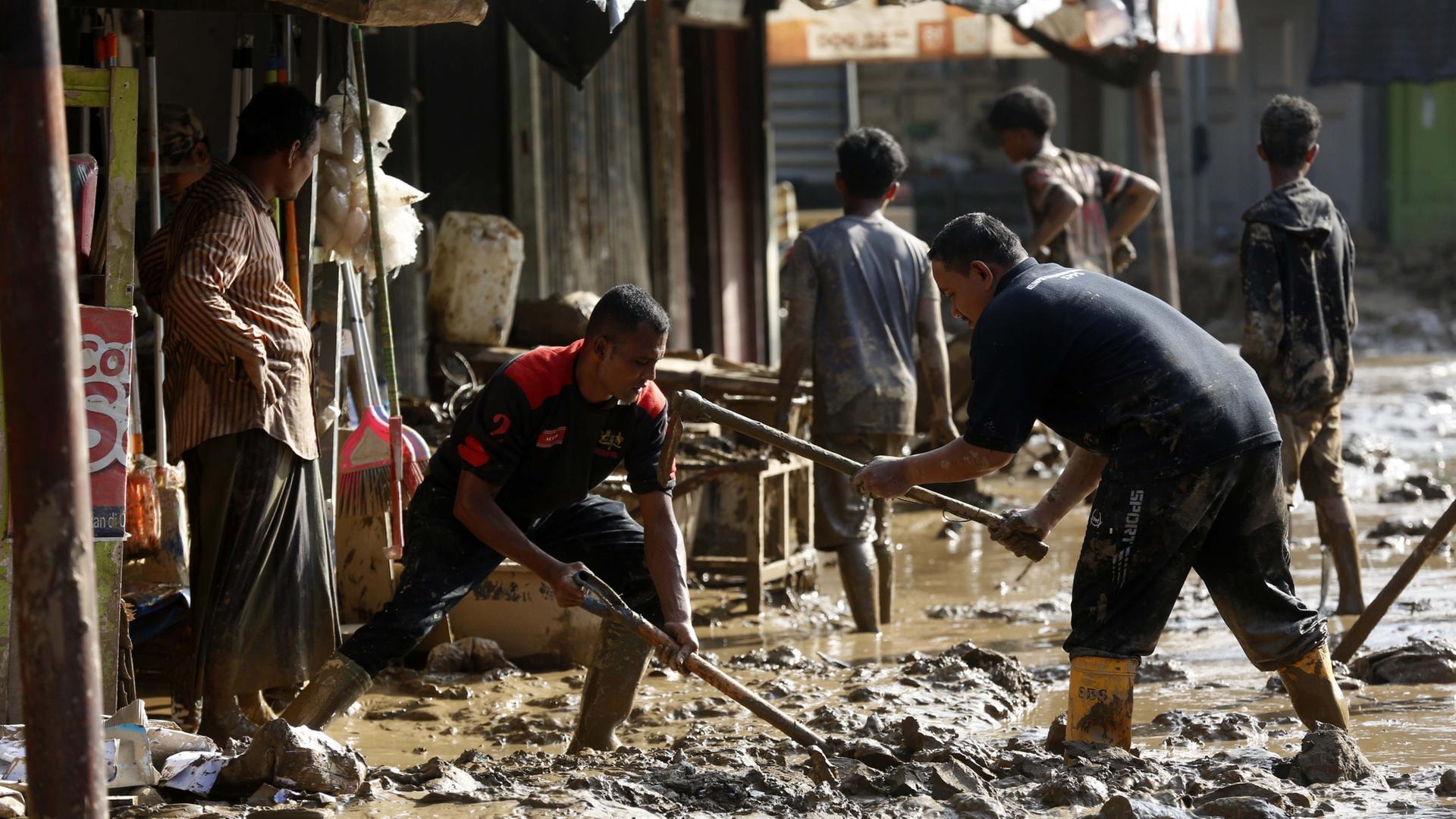 Menschen arbeiten mit Spitzhacken in einer von Schlamm überfluteten Straße | EPA