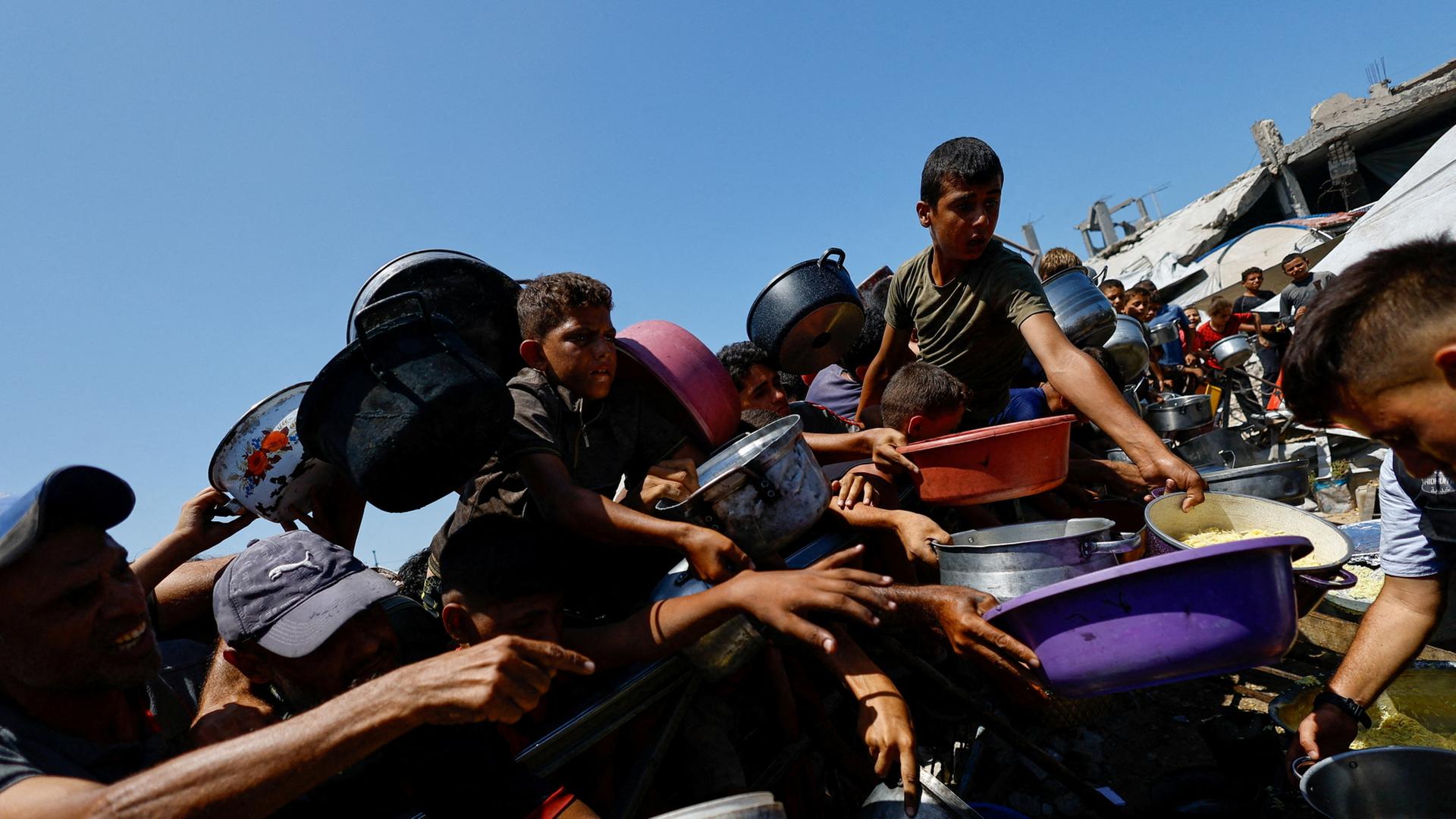 Menschen im Gazastreifen drängen sich mit Schüsseln um eine Essensausgabe. | REUTERS