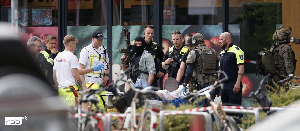 Einsatzkräfte stehen vor einem Supermarkt neben einer verletzten Person auf einer Trage. (Quelle: dpa/Carsten Koall)