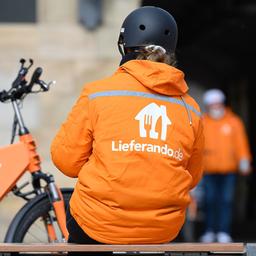 Lieferando Fahrradkurier sitzt neben seinem Rucksack