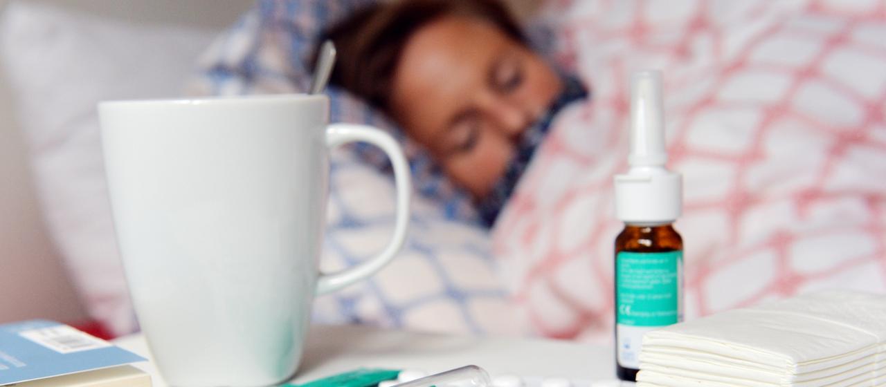 Fieberthermometer, Medikamente und Teetasse stehen auf einem Nachttisch.