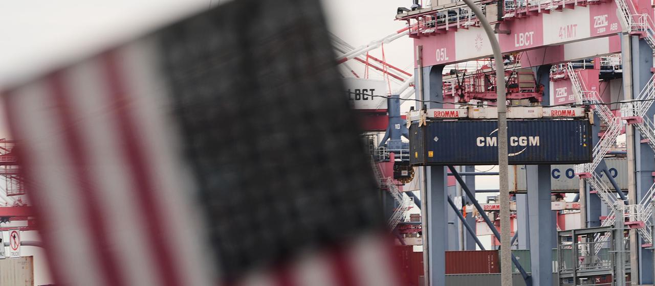 Vor einem Containerterminal ist eine Flagge der USA zu sehen.