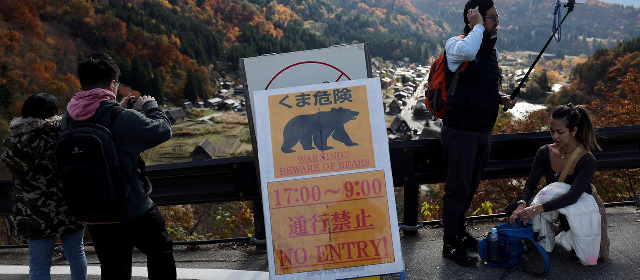 Besucher machen Erinnerungsfotos neben einem Warnschild für Bären in Shirakawa-go, Japan.