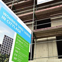 Projekttafel für Wohnungsbau in Citylage vor einem Rohbau.
