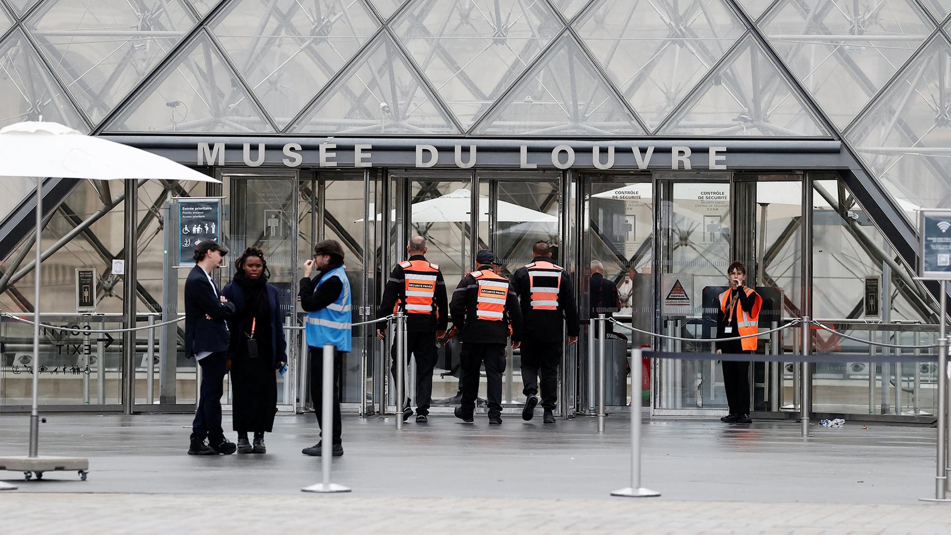 Mehrere Sicherheitskräfte in orangefarbenen Westen stehen vor dem Eingang des Louvre in Paris. | REUTERS
