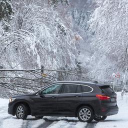 Ein Auto steht auf einer verschneiten Straße. Ein umgestürzter Baum verhindert die Weiterfahrt.