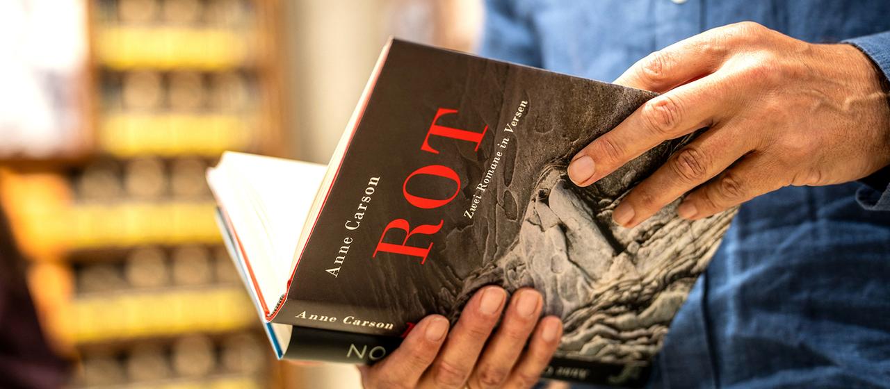 Ein Mann hält ein Buch von Anne Carson in der Hand.