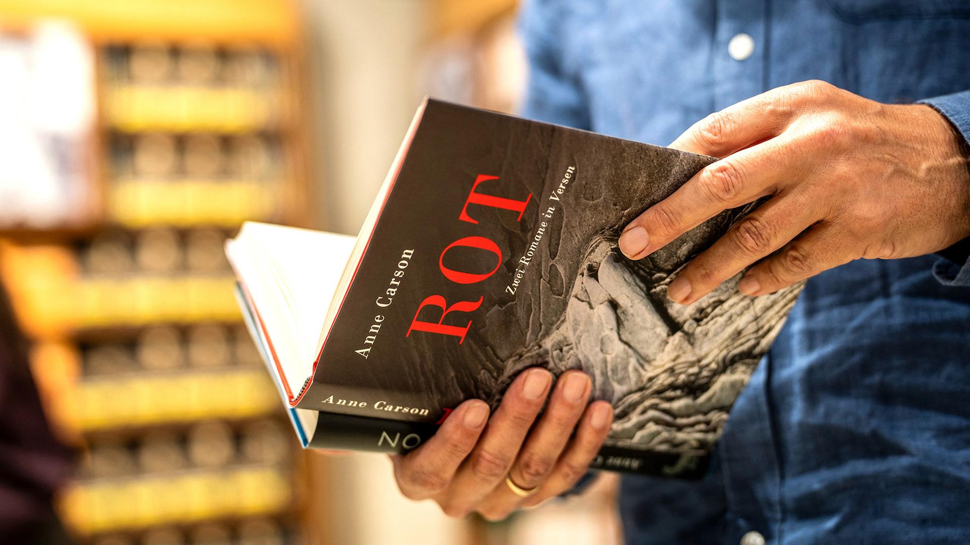 Ein Mann hält ein Buch von Anne Carson in der Hand. | picture alliance/dpa