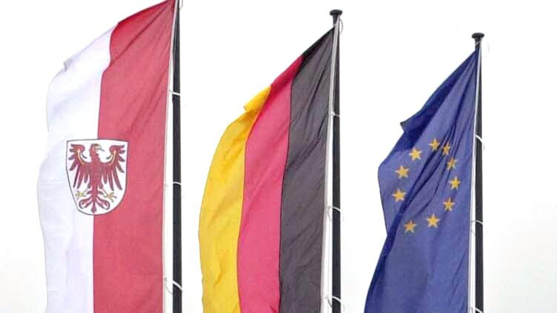 Landesfahne Brandenburg, die Deutschlandfahne und die Europafahne, aufgenommen vor einem Gebäude in Neuruppin (Quelle Archivbild: Zentralbild/Nestor Bachmann)  | Zentralbild/Nestor Bachmann